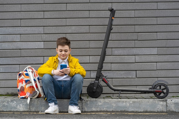 Adolescente con teléfono móvil sentado cerca de su scooter eléctrico