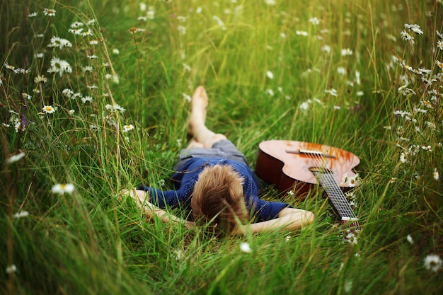 Adolescente tirado en el pasto con su guitarra acústica