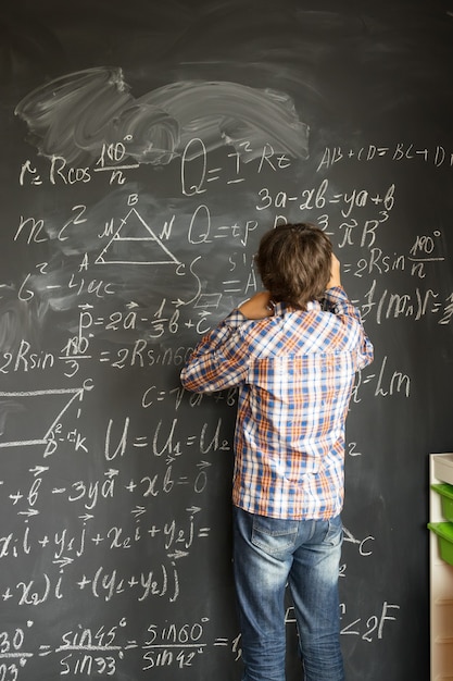 Adolescente con tiza escribiendo complicadas fórmulas matemáticas en la pizarra