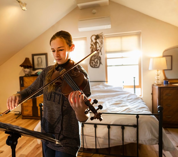 Adolescente tocando su violín en su dormitorio