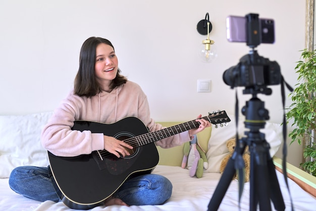 Adolescente tocando violão, conversando com seguidores, gravando vídeo para canal, blog. Hobbies para meninas, música, arte, educação, comunicação online com crianças e adolescentes