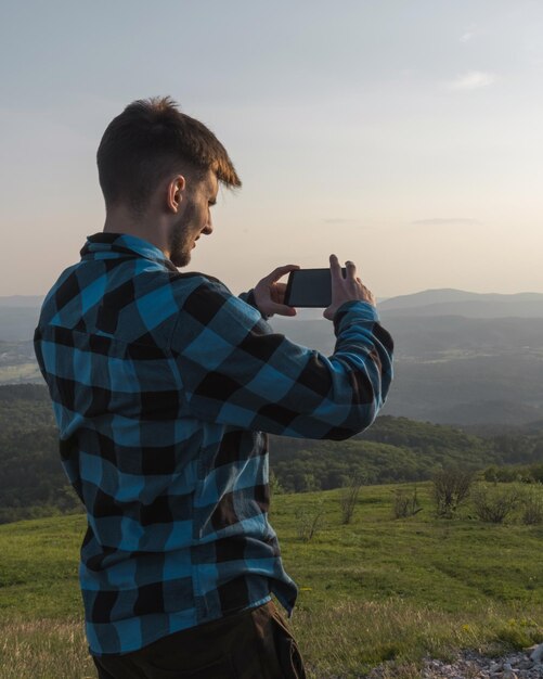 Adolescente tomando fotos del fantástico paisaje montañoso al atardecer con su teléfono inteligente