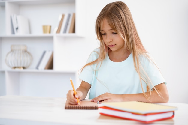 Adolescente tomando notas en el bloc de notas haciendo los deberes en la mesa en casa