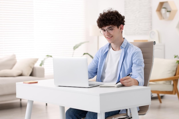 Adolescente tomando notas mientras trabaja con una computadora portátil en el sofá en casa Trabajo remoto