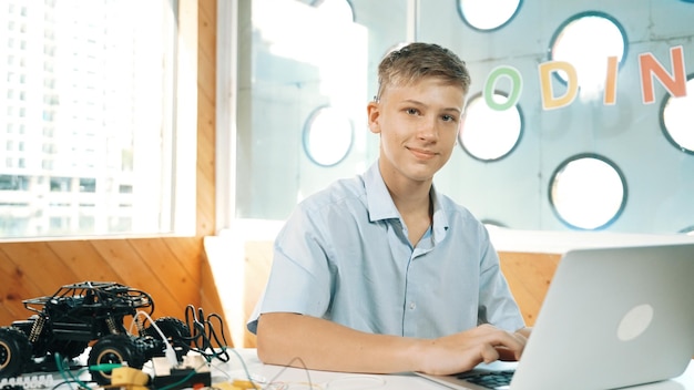 Foto adolescente trabajando en una computadora portátil y mirando a la cámara en la clase de stem edificación