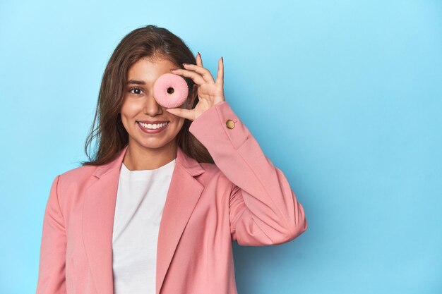 Adolescente con traje rosa sosteniendo rosquillas ante los ojos sonriendo