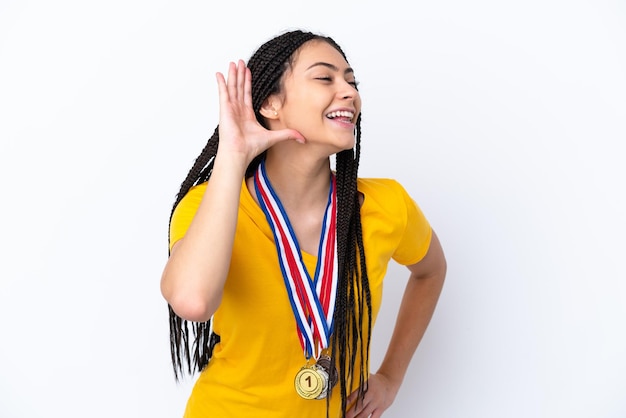 Adolescente con trenzas y medallas sobre un fondo rosa aislado escuchando algo poniendo la mano en la oreja