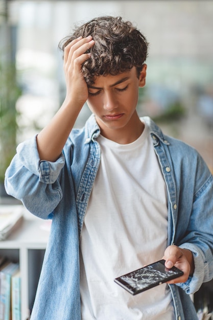 Foto adolescente triste e estressado segurando um telefone celular com tela quebrada
