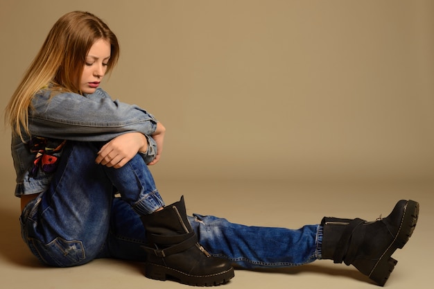 Adolescente triste sentada no chão com sapatos de jaqueta jeans