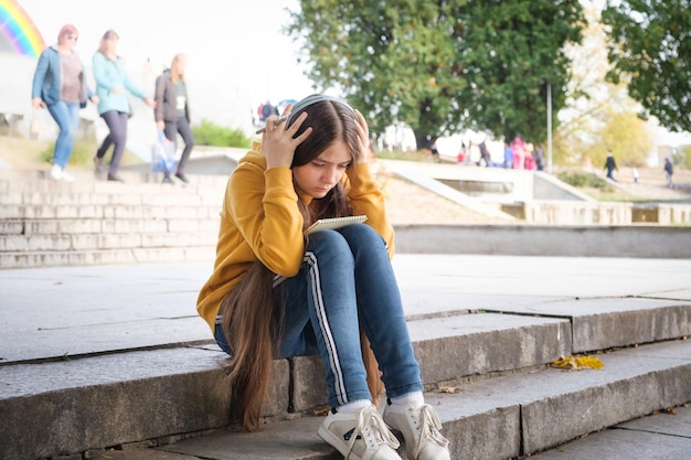 Foto una adolescente triste se sienta en las escaleras y se cubre la cabeza con las manos.