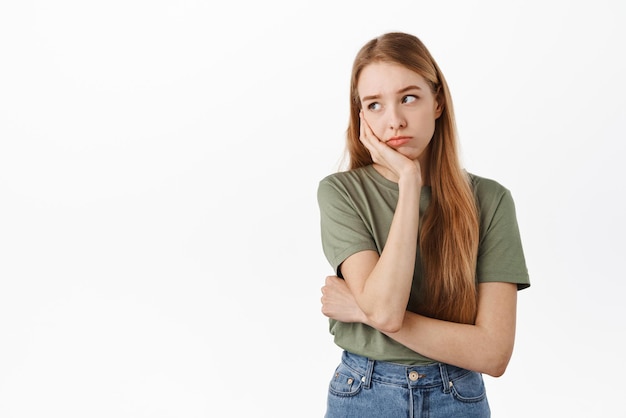 Una adolescente triste y sombría mirando a un lado apoyándose en la mano con expresión de cara aburrida no tiene nada que hacer en cuarentena de pie contra fondo blanco