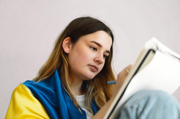 Foto una adolescente ucraniana está envuelta en la bandera ucraniana y está dibujando o haciendo tareas