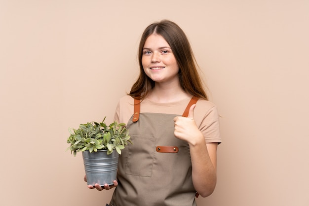 Adolescente ucraniana jardinero chica sosteniendo una planta dando un gesto de pulgares arriba