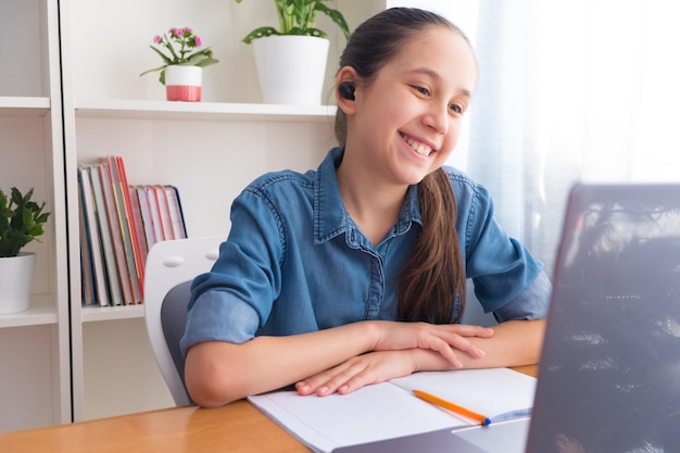 Adolescente usa auriculares inalámbricos para estudiar en la computadora en casa, hace la tarea en Internet