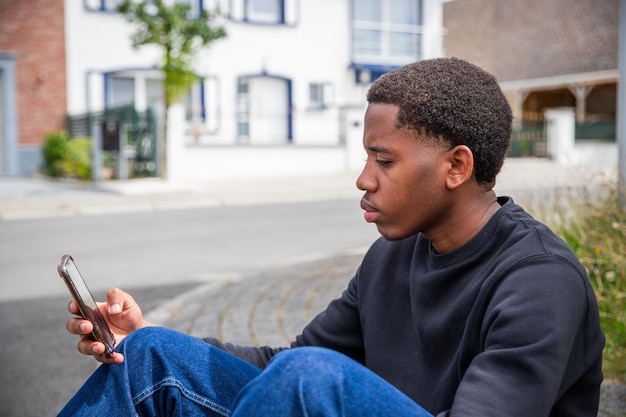 Un adolescente usa su teléfono inteligente sentado en la acera conectado a jóvenes