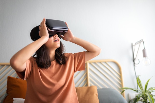 Adolescente usando fone de ouvido VR em casa Estupefacta jovem asiática usando óculos de realidade virtual