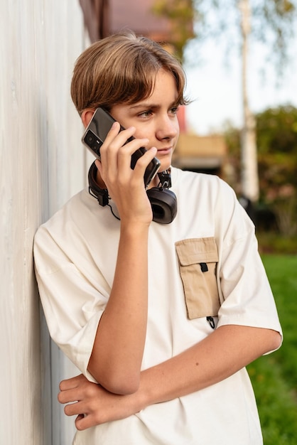 Foto adolescente usando fones de ouvido e falando ao telefone conversando ao ar livre criança usando telefone celular conversas ao ar livre adolescente falando no smartphone
