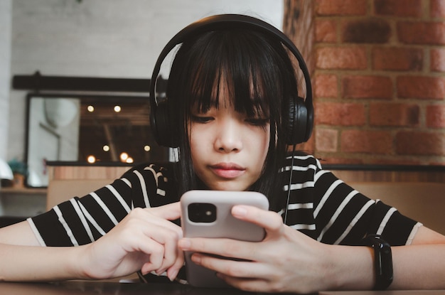 Adolescente usando fones de ouvido e segurando uma mídia social de smartphone celular relaxando no sofá