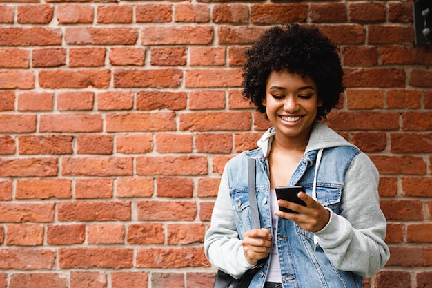 Adolescente usando telefone celular enquanto está de pé contra uma parede de tijolos