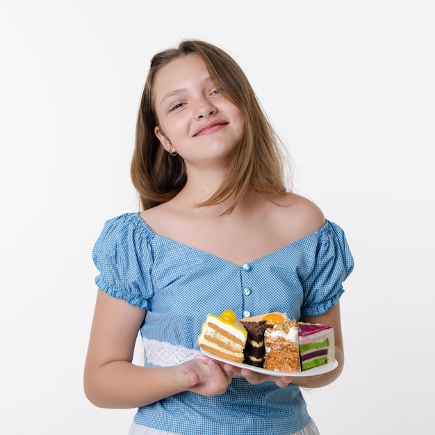 Adolescente con vestido azul sostiene un plato de pasteles dulces de crema y sonríe Retrato de estudio en blanco