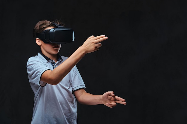 Adolescente vestido con una camiseta blanca jugando con gafas de realidad virtual. Aislado en un fondo oscuro.