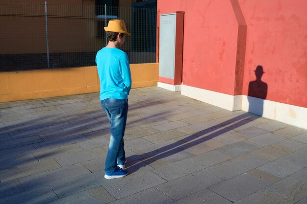 Adolescente vistiendo sombrero amarillo fedora y camisa turquesa mira su larga sombra. Tarde en la isla de Burano en la laguna de Venecia, en el norte de Italia.