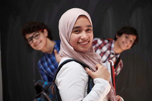Adolescentes árabes, retrato de grupo de estudiantes contra pizarra negra con mochila y libros en la escuela