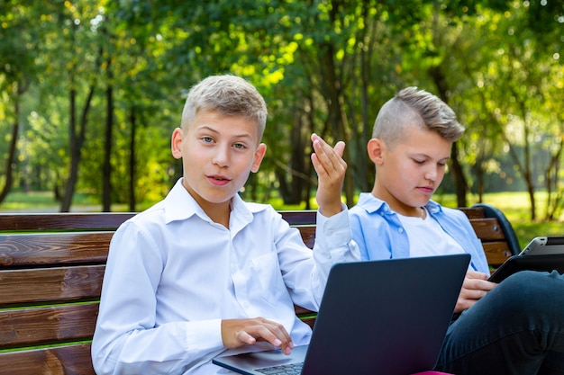 Adolescentes en el banco del parque con ordenador portátil y tableta digital