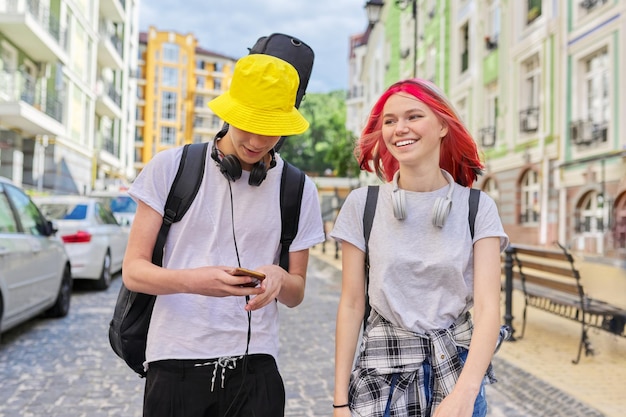 Adolescentes cara e garota andando e conversando ao longo da rua da cidade com guitarra no caso