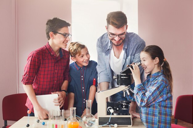 Adolescentes com professor fazendo experimento químico em laboratório com reagentes e olhando através de um microscópio. Desenvolvimento inicial, educação, diy, conceito de inovação. Educação de tronco.