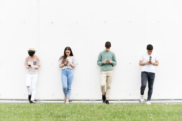 Adolescentes contra la pared usando teléfonos