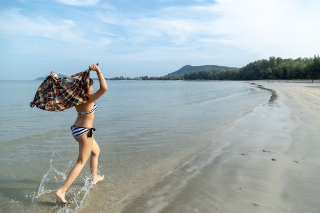 Adolescentes da Ásia vestindo biquíni correndo na praia ao fundo do mar é um céu azul.