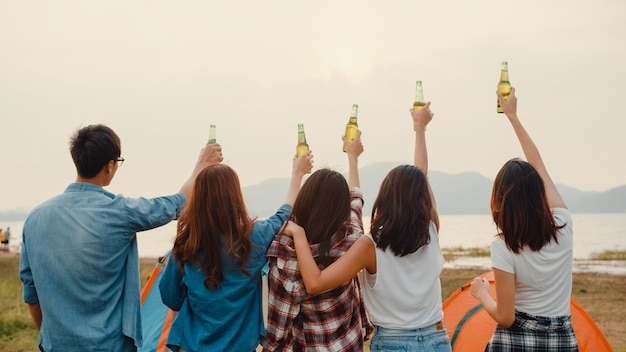 Foto adolescentes do grupo de melhores amigos da ásia saúdam e gritam brinde de cerveja em garrafa, festejam com momentos felizes juntos no acampamento do parque nacional