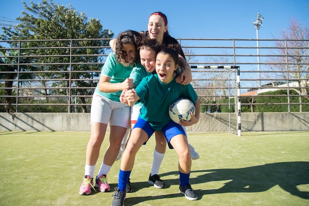 Adolescentes durante o treinamento de futebol. Equipe de quatro garotas rindo pulando umas nas outras, sentindo alegria e mostrando seus punhos e união para a vitória. Esporte de equipe, hobby, conceito de futebol feminino