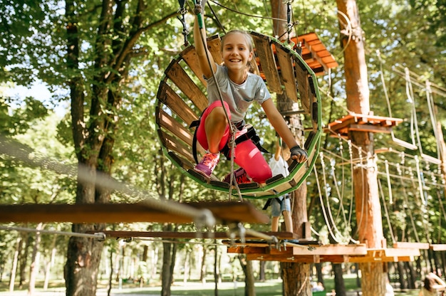 Adolescentes em escaladas de equipamento em parque de corda, playground. Crianças subindo em ponte suspensa