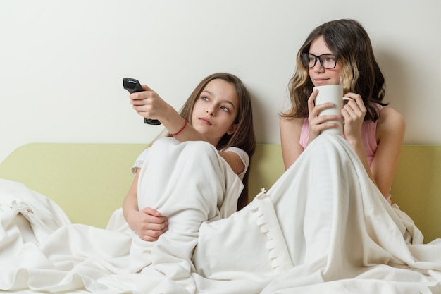 Las adolescentes están sentadas en casa en la cama y viendo la televisión.