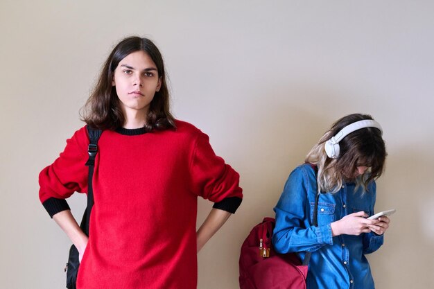 Adolescentes estudiantes chico y chica con mochilas en el fondo de la pared de luz