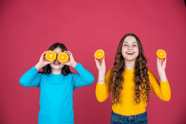 Las adolescentes felices sostienen fruta naranja sobre fondo rosa