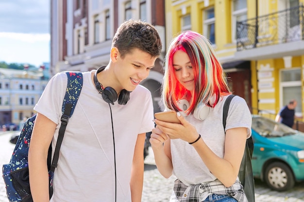 Adolescentes guapos pareja chico y chica juntos en la calle de la ciudad mirando en la pantalla del teléfono inteligente