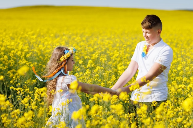 Adolescentes hermano y hermana con corona ucraniana en la cabeza en campo de colza bajo un cielo azul