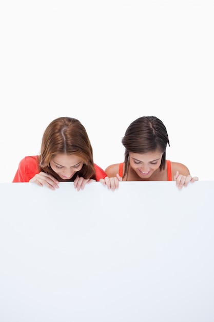 Foto adolescentes mirando un cartel en blanco mientras se inclina la cabeza hacia adelante