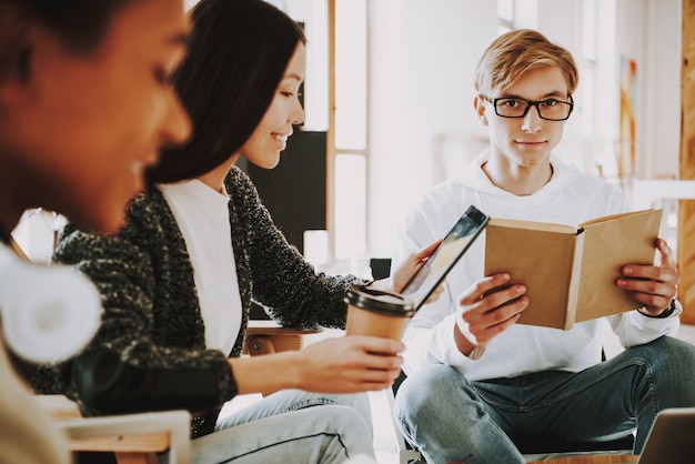 Adolescentes novos que sentam-se nas poltronas no lugar de coworking.