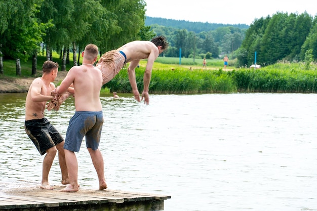 Los adolescentes saltan al agua y nadan en el lago en un caluroso día de verano Recreación activa en un estanque abierto Los niños saltan al agua y realizan trucos acrobáticos