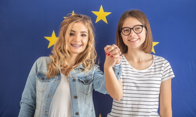 Adolescentes sorridentes estão de mãos dadas com uma bandeira da ue atrás delas.