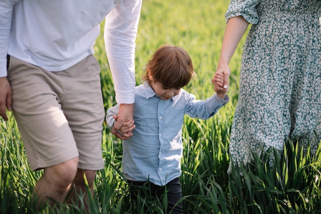 Adopción y concepto de infancia feliz, papá, mamá e hijo tomados de la mano y caminar sobre la hierba verde