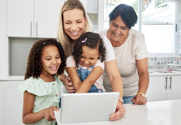 Foto adopción familiar combinada y una niña con su madre en una tableta en la cocina para educación o aprendizaje diversidad de niños o estudio con un padre y una abuela enseñando a niñas en casa juntas