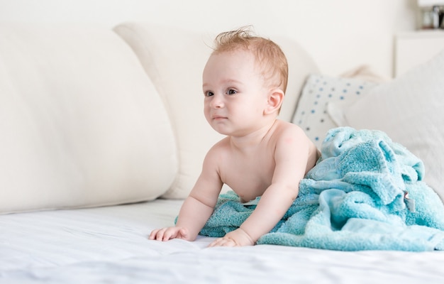 Adorable Baby Boy después de la ducha cubierto con una manta azul en el sofá en la sala de estar