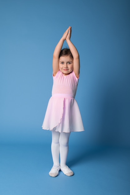 Adorable bailarina en vestido rosa se para y levanta los brazos estirando así su cuerpo.