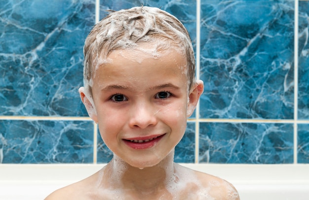 Adorable bebé con espuma de jabón de champú en el pelo tomando baño. Closeup retrato de niño sonriente, cuidado de la salud y el concepto de higiene como logotipo. Aislado en fondo blanco y azul con trazado de recorte.