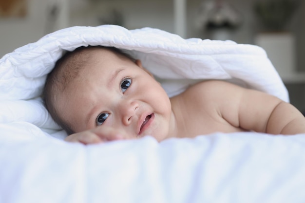 Adorable bebé gateando sobre el cuerpo de la cama cubierto por la manta Momentos felices